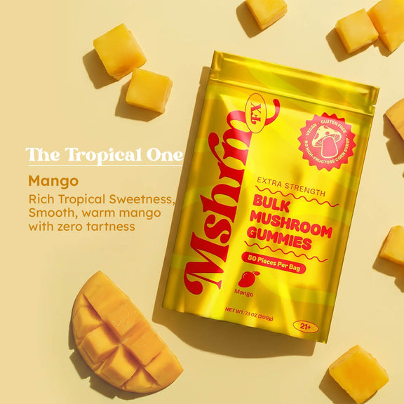 MshrooM FX Extra Strength Bulk Mushroom Gummies Mango 50 count yellow bag flat lay on cream background surrounded by fresh cut mango cubes and a scored mango half with The Tropical One flavor callout describing rich tropical sweetness, smooth warm mango with zero tartness, showing vegan, gluten free, no high fructose corn syrup badge, 21 plus age requirement, and 7.1 oz net weight.
